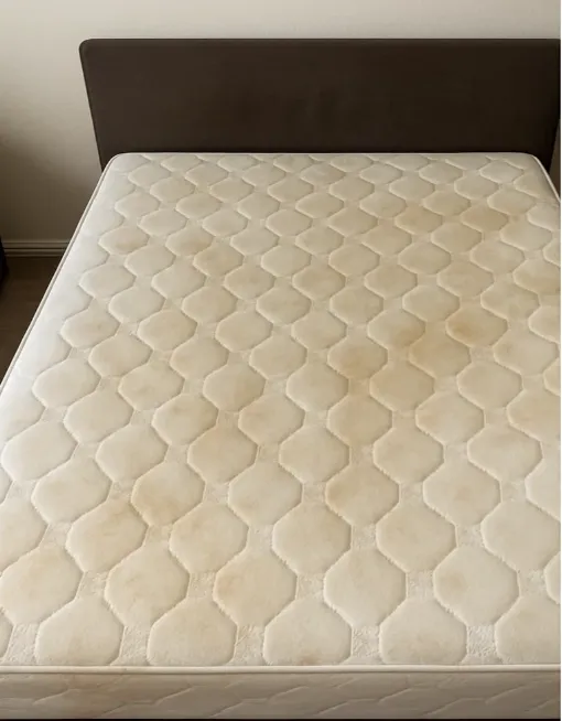 A mattress with visible yellow sweat stains and discolouration before professional cleaning.